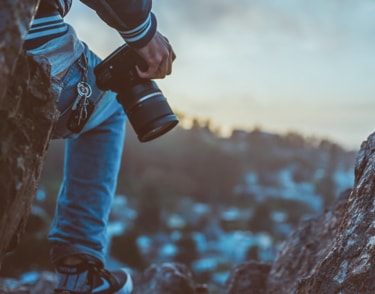 Silhouette of a man on top of rocks with a camera resting on his right knee