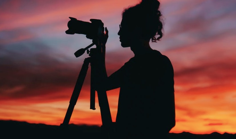 A lady standing in a field whilst taking a picture at dusk