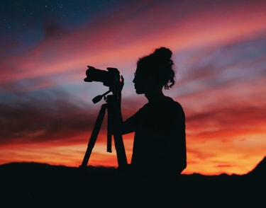 A lady standing in a field whilst taking a picture at dusk
