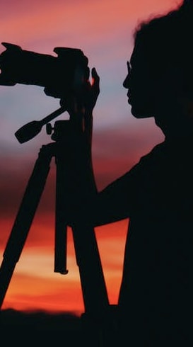 A lady standing in a field whilst taking a picture at dusk